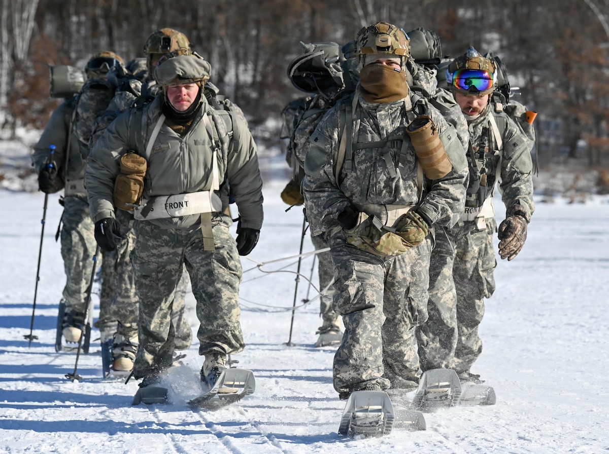 Air National Guard Security Forces specialists ruck across a frozen lake in full winter uniforms wearing snowshoes and utilizing trekking poles.
