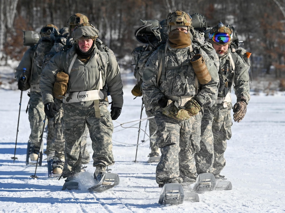 Air National Guard Security Forces specialists ruck across a frozen lake in full winter uniforms wearing snowshoes and utilizing trekking poles.