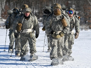 Air National Guard Security Forces specialists ruck across a frozen lake in full winter uniforms wearing snowshoes and utilizing trekking poles.