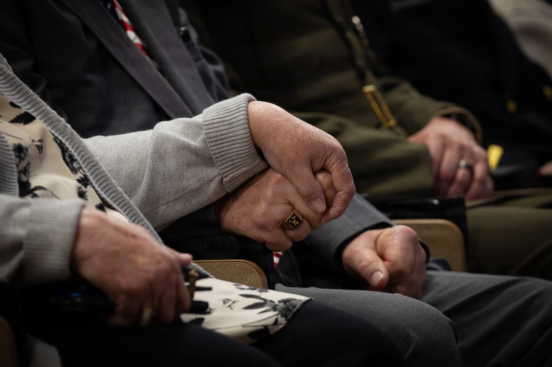 Allan McPherson, brother of the late Maj. Everette McPherson, holds the hand of his wife during a posthumous Distinguished Flying Cross ceremony honoring the heroic actions of his brother at Marine Support Facility New Orleans, March 18, 2026. The Distinguished Flying Cross is awarded to those who have displayed single acts of heroism or extraordinary achievement while participating in aerial flight. Maj. McPherson, a fighter jet pilot, posthumously received the award for sacrificing his life during the Vietnam War in an attempt to save the life of his co-pilot. (U.S. Marine Corps photo by Lance Cpl. Claire Cheney)