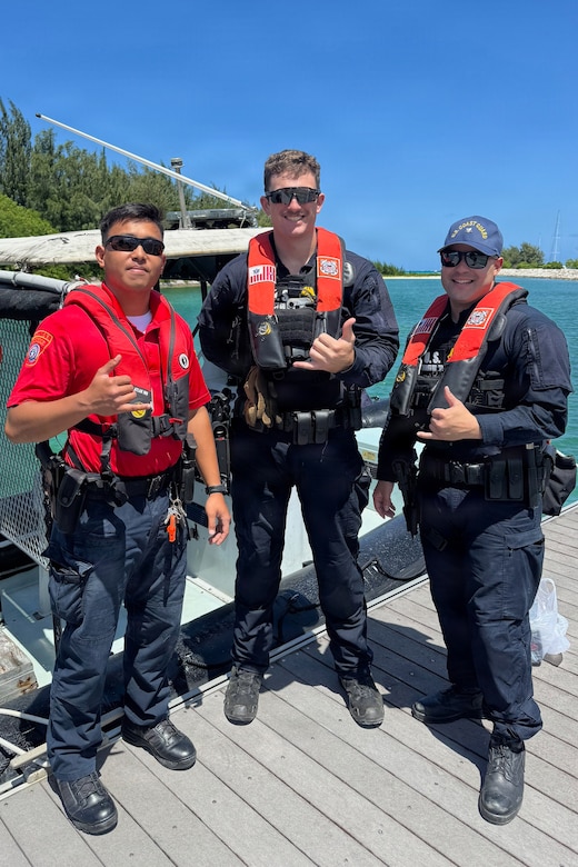 Three men wearing life jackets and sunglasses pose for a photo on a pier with a small boat moored in the background.
