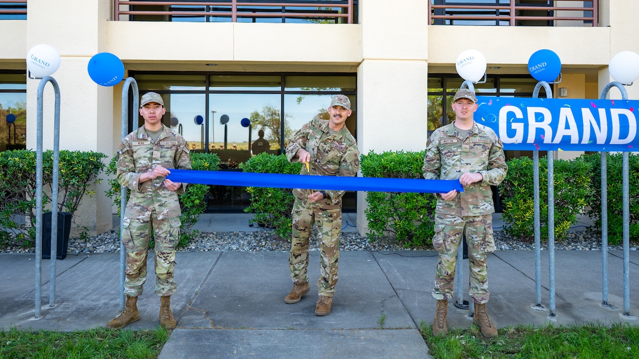 Airmen hold a ribbon while a commander cuts it