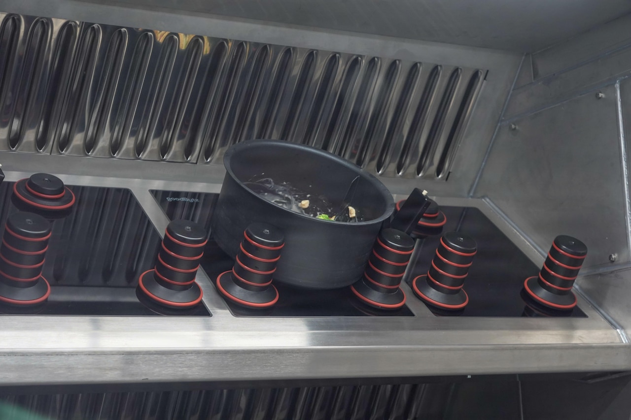 A bowl of boiling water and ingredients sits on a stove in an outdoor, mobile military kitchen.