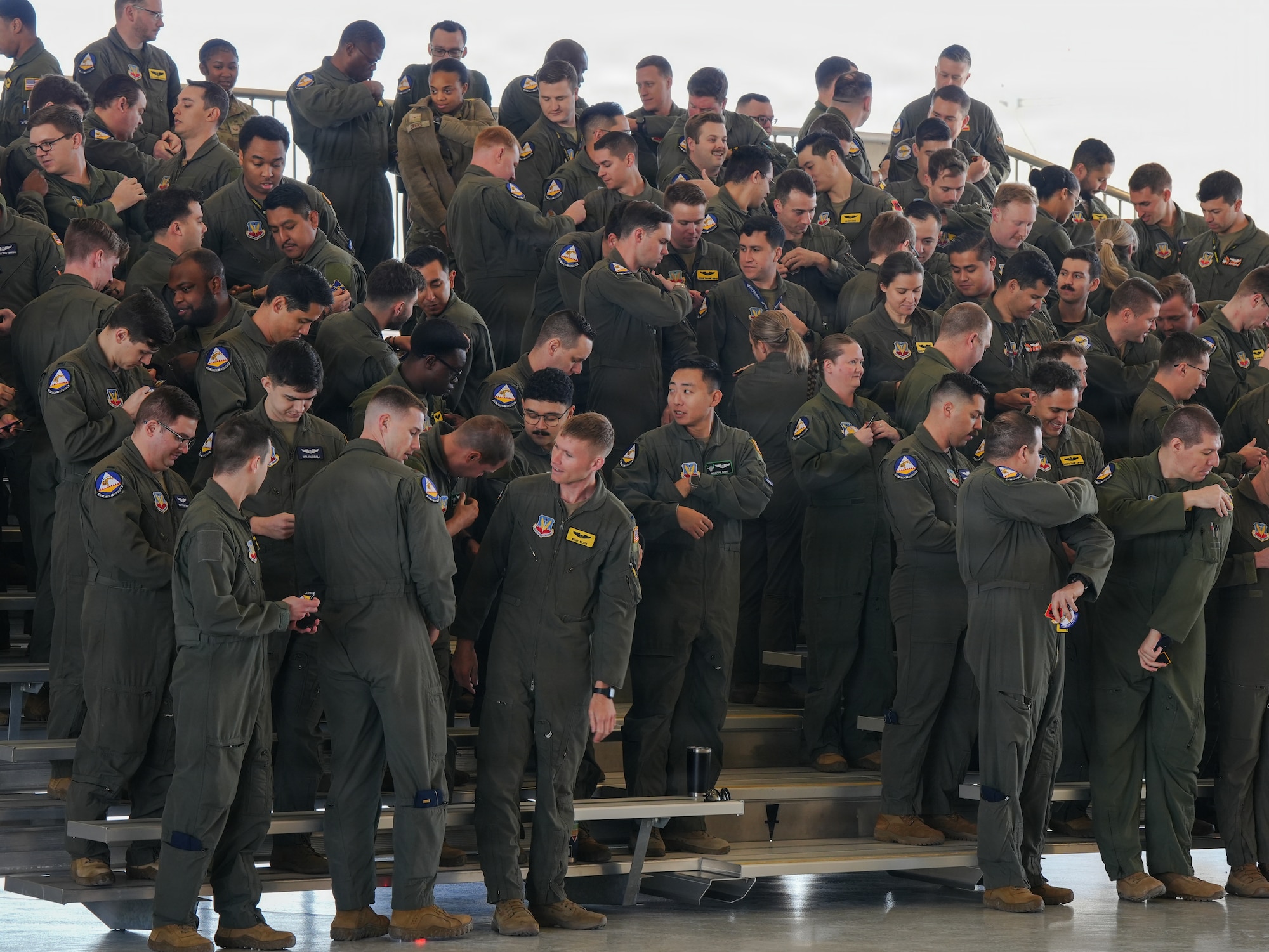 A crowd of U.S. Air Force members in flight suits are standing on bleachers and replacing their patches with new patches.