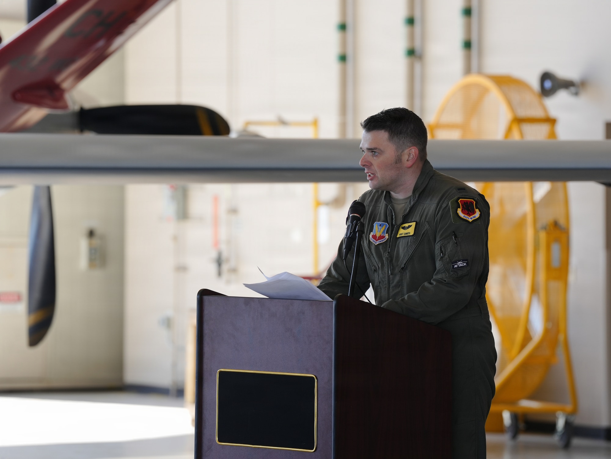 A U.S. Air Force Lt. delivers remarks from a podium in an aircraft hangar.