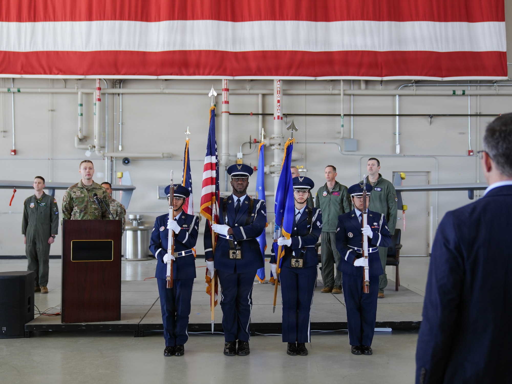 Four U.S. Air Force Honor guard members hold the American and U.S. Air Force Flags on a stage in an aurcraft hangar.