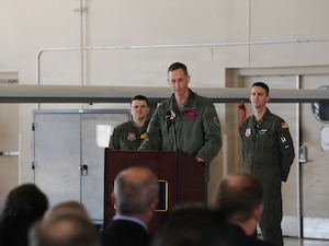 A U.S. Air Force Col. delivers remarks from a podium in an aircraft hangar.