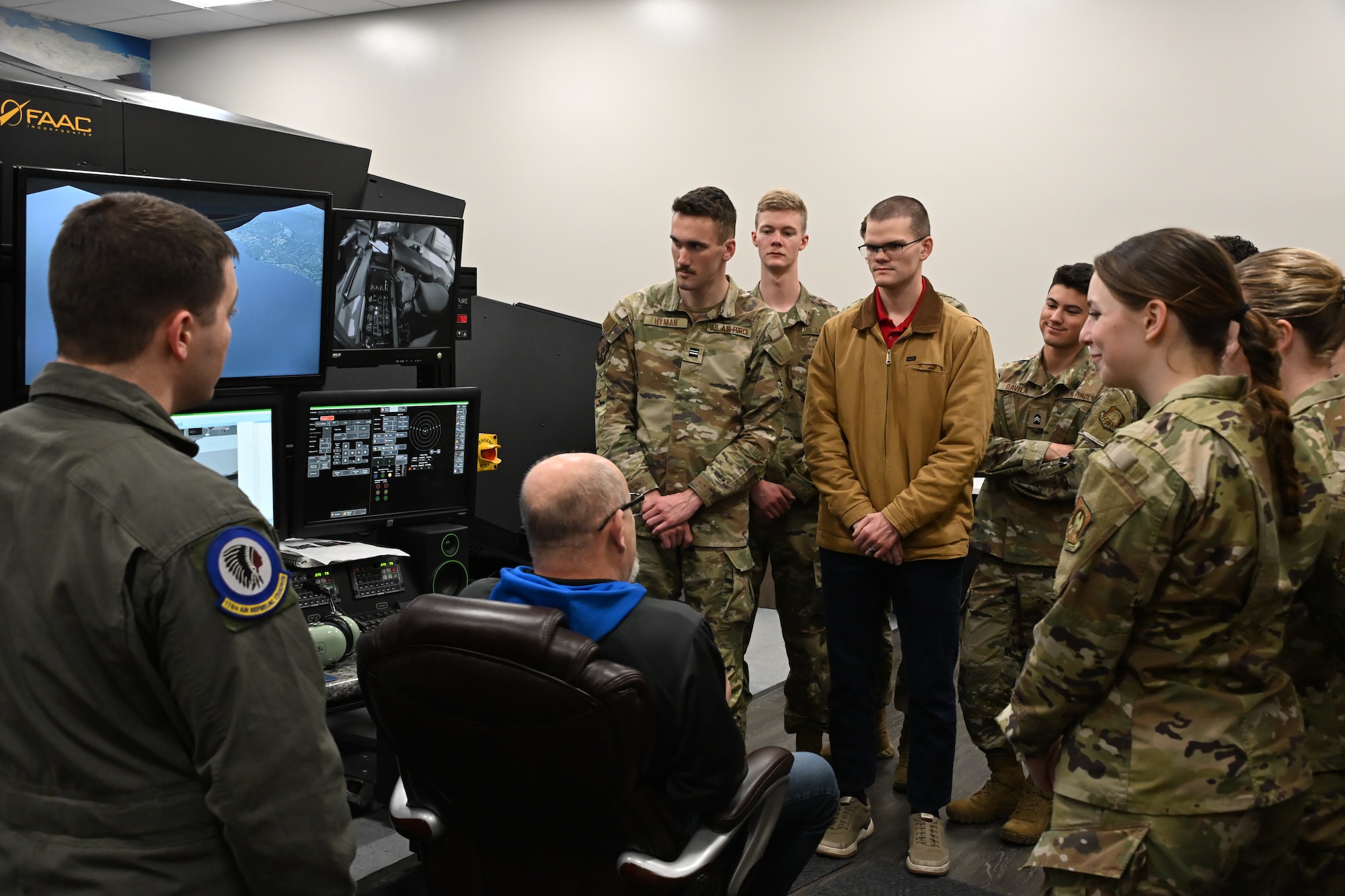 Jay Doran, a simulator technician, is seat and surrounded by U.S. Air Force Reserve Officers’ Training Corps cadets next to monitors for an air-refueling simulator.