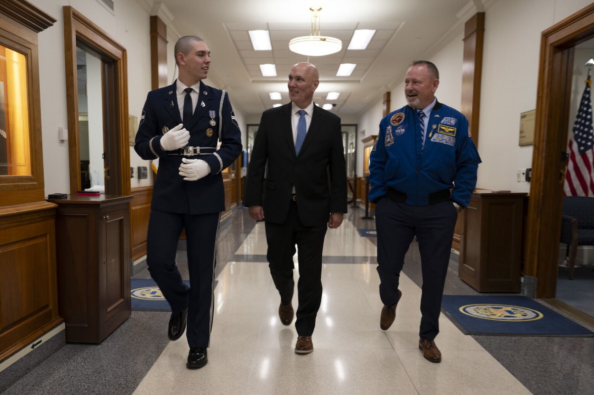 Three men walk alongside each other down a hallway.