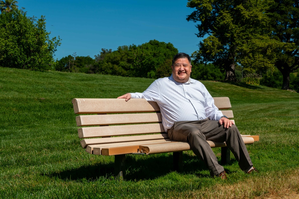 Man sits on bench on a sunny day with a bright blue sky