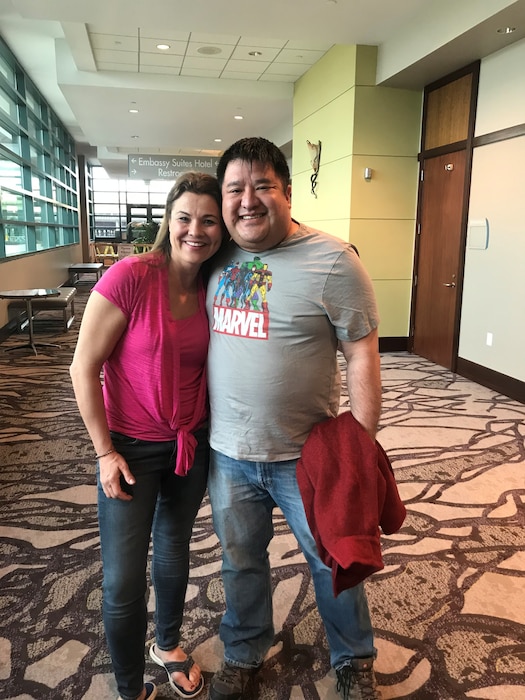 A man and woman pose together for a photograph in a hallway.