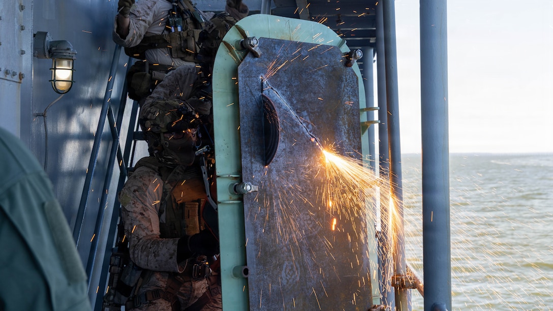 U.S. Marines with Maritime Reconnaissance Force, 24th Marine Expeditionary Unit, cut through a metal door while conducting visit, board, search, and seizure training on the James River, Virginia, March 18, 2026. VBSS training equips personnel with the skills necessary to effectively conduct maritime operations, focusing on safety, security, and compliance during boarding missions. (U.S. Marine Corps photo by Cpl. Daniel R. Garcia)