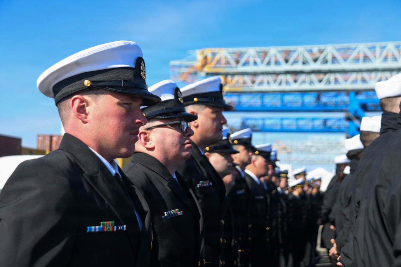 Dozens of people in military dress uniforms stand outside in formation.