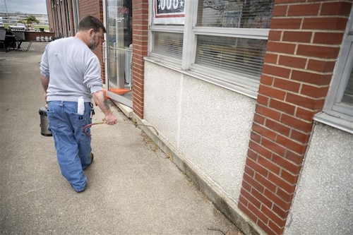 A pest management specialist applies treatment along the exterior of a building at Wright-Patterson Air Force Base to control ants and prevent pest-related health risks.