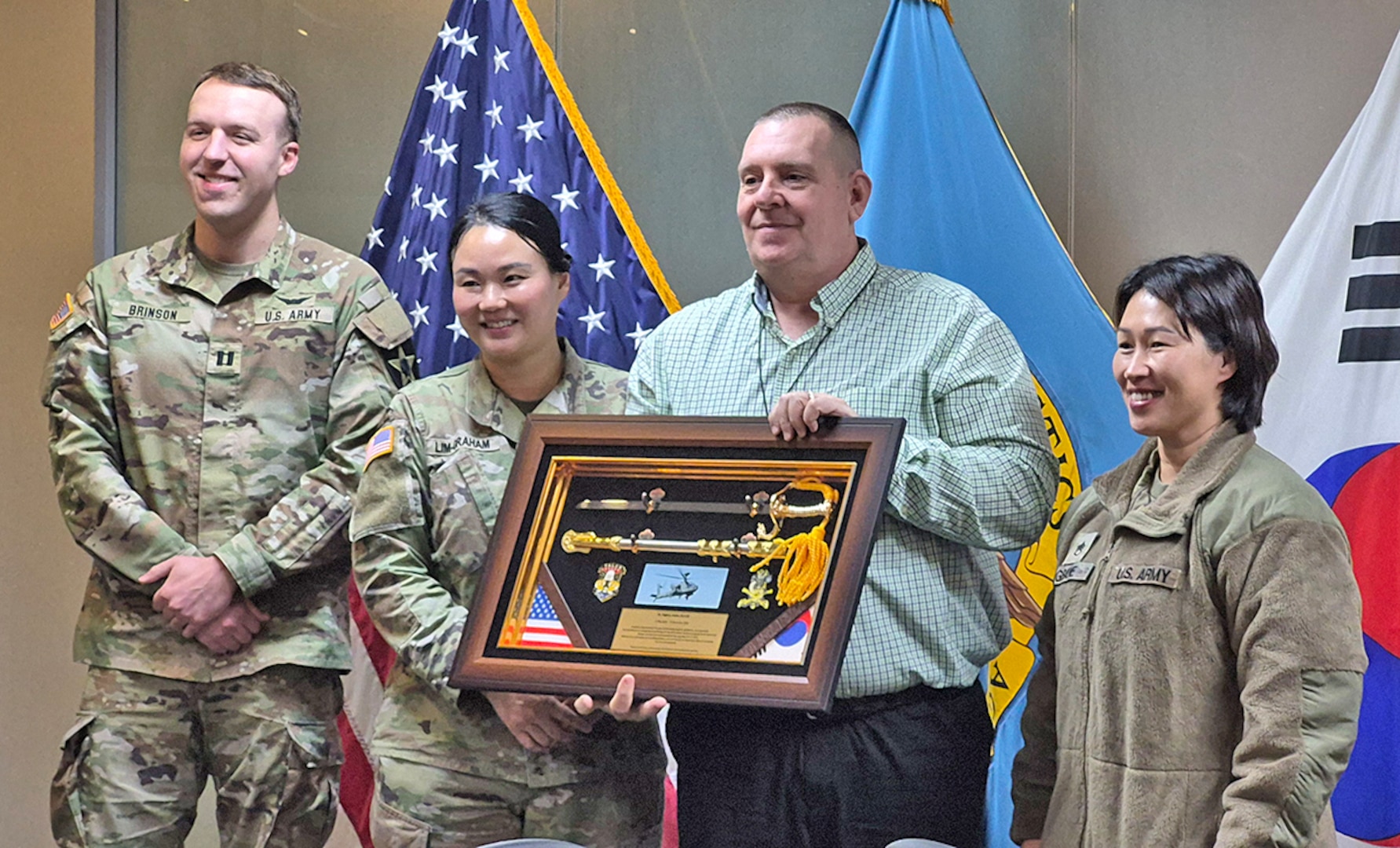 A man holds a shadow box in front of flags while posing with three soldiers.