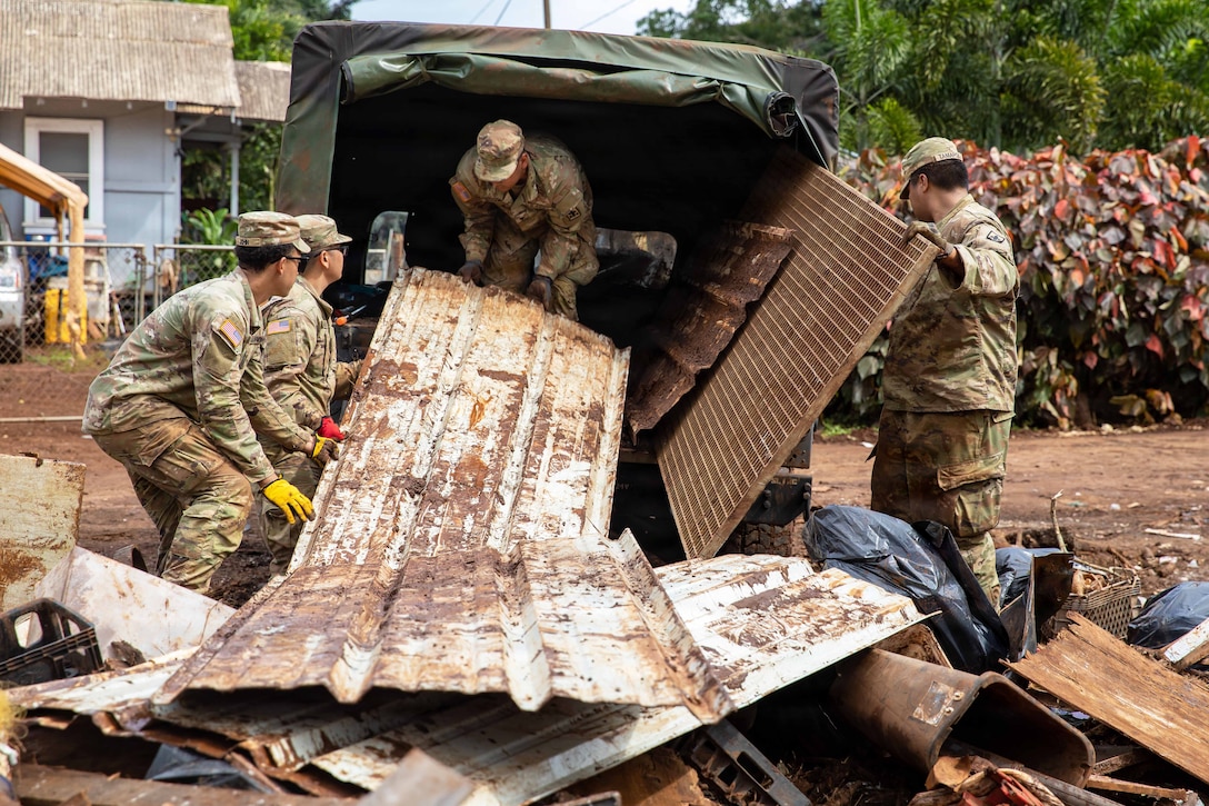 Four National Guardsmen lift debris into the back of a vehicle near a house.
