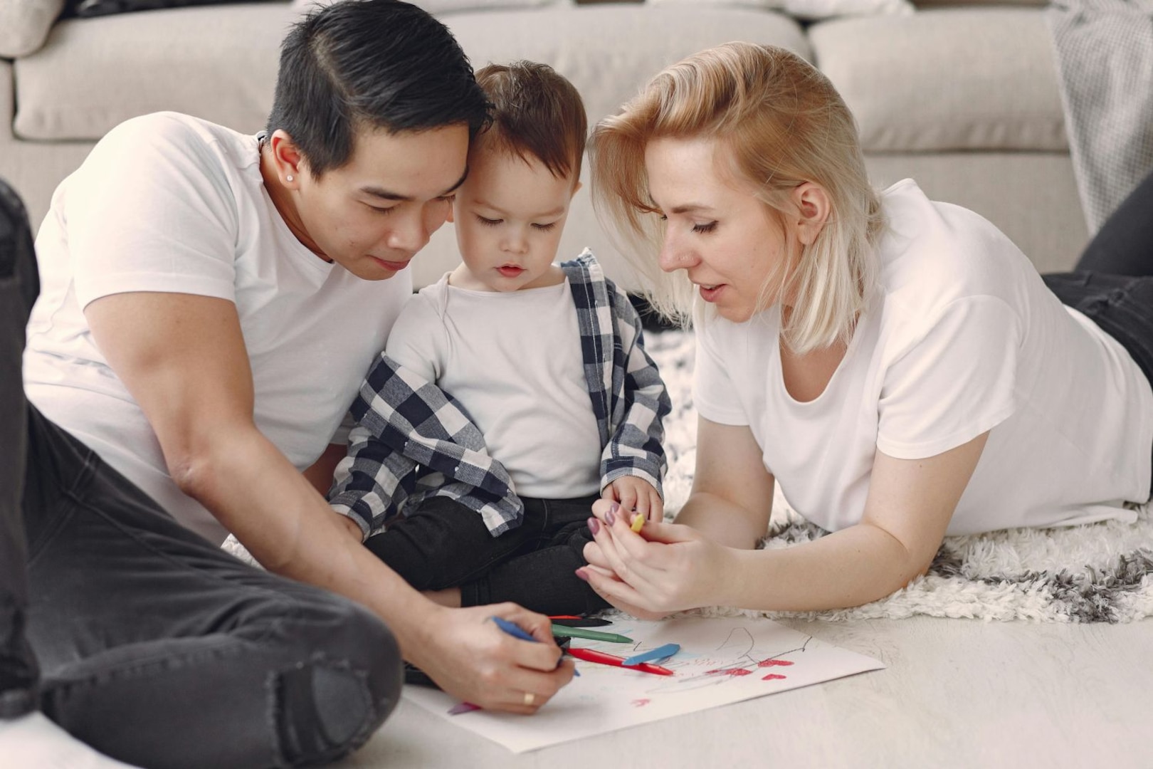 Man and woman draw on a piece of paper with a toddler in between them.