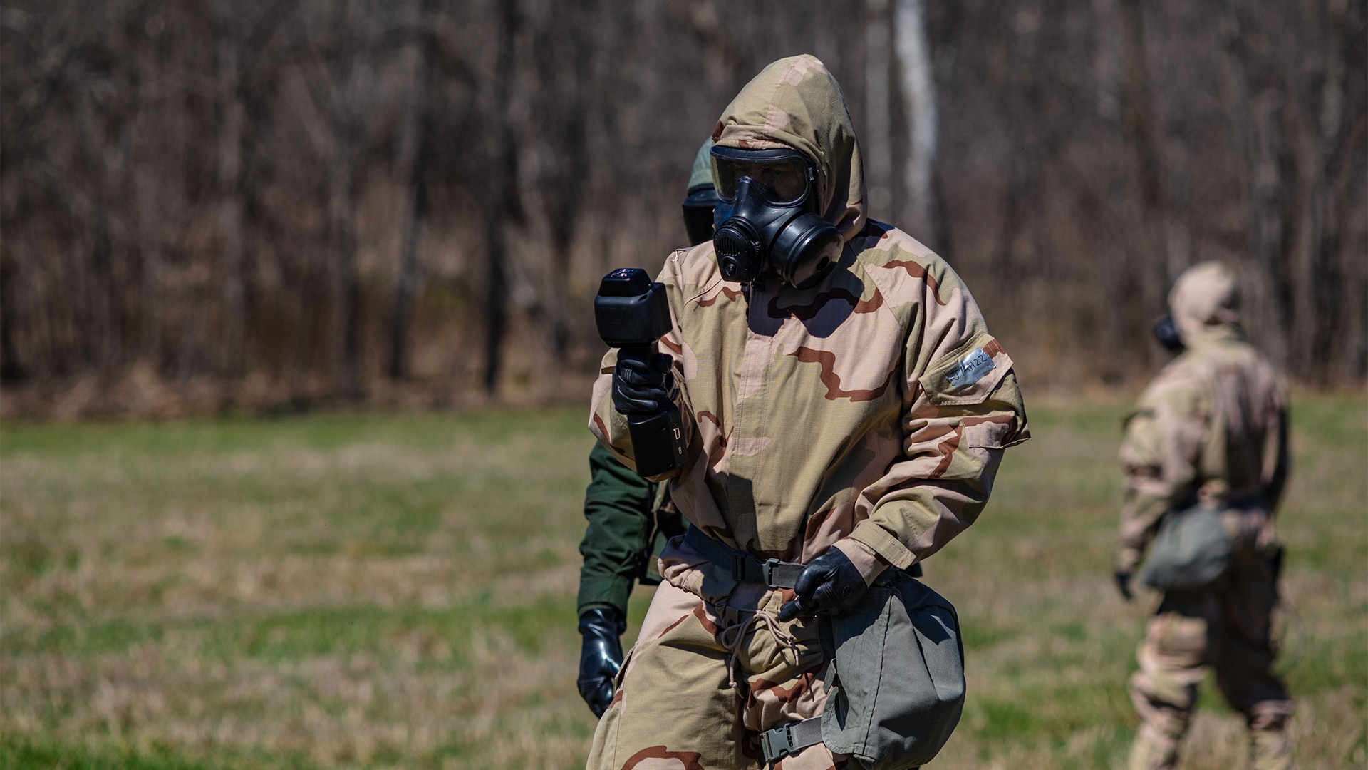 Military member in full mopp suit with sensor device in a field.