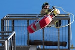 U.S. Army Spc. Michael Conrad, 416th Theater Engineer Command firefighter, hoists a fire hose roll to the top of the four-story training tower during the Iron Mike competition at Joint Base San Antonio-Randolph, Texas, March 18, 2026. The 50-pound hose roll tested firefighters’ strength and endurance as the last station of a relay event. (U.S. Air Force photo by Airman 1st Class Kevin Jones)