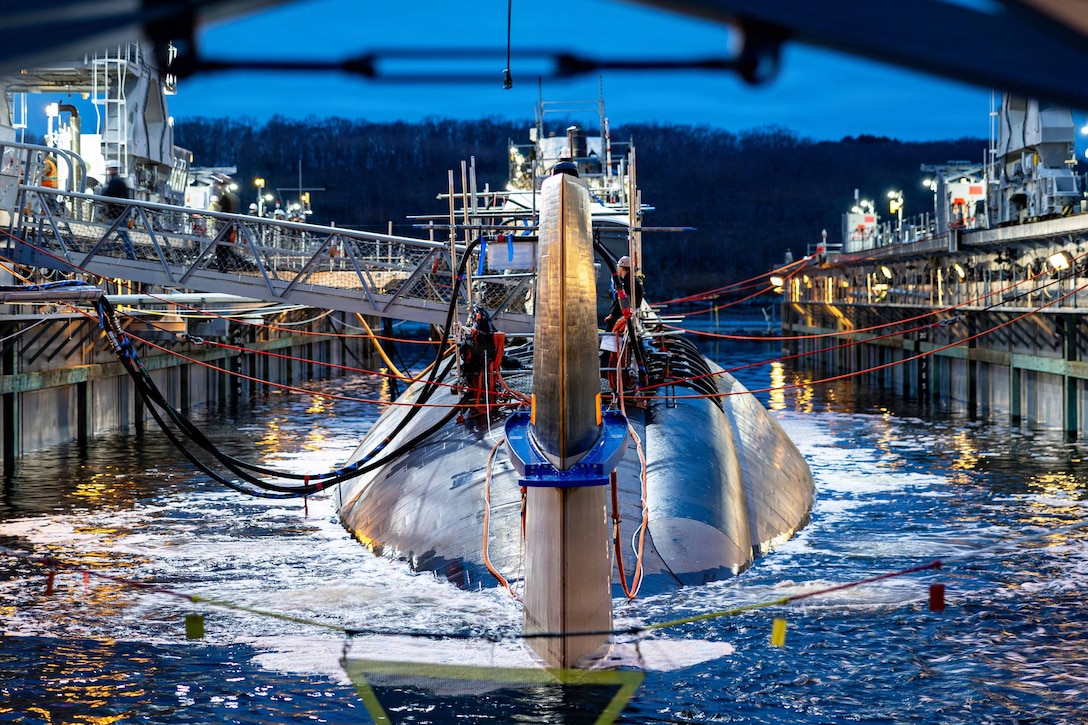 A submarine sits in between two docks connected by several cords with trees in the background.