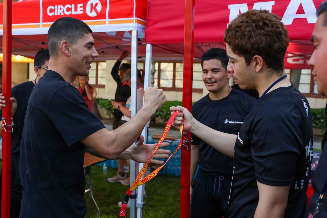 U.S. Marine Corps poolees with Recruiting Sub-Station Corona, Recruiting Station Riverside, interact with an event attendee during the Corona 5000 Road Race at the Corona Historic Civic Center in Corona, California, March 21, 2026. The Corona 5000 Road Race was designed to bring the community together for fitness and showcase the city by using the historic 3-mile Grand Boulevard loop. (U.S. Marine Corps photo by Lance Cpl. Monserrath Mora)