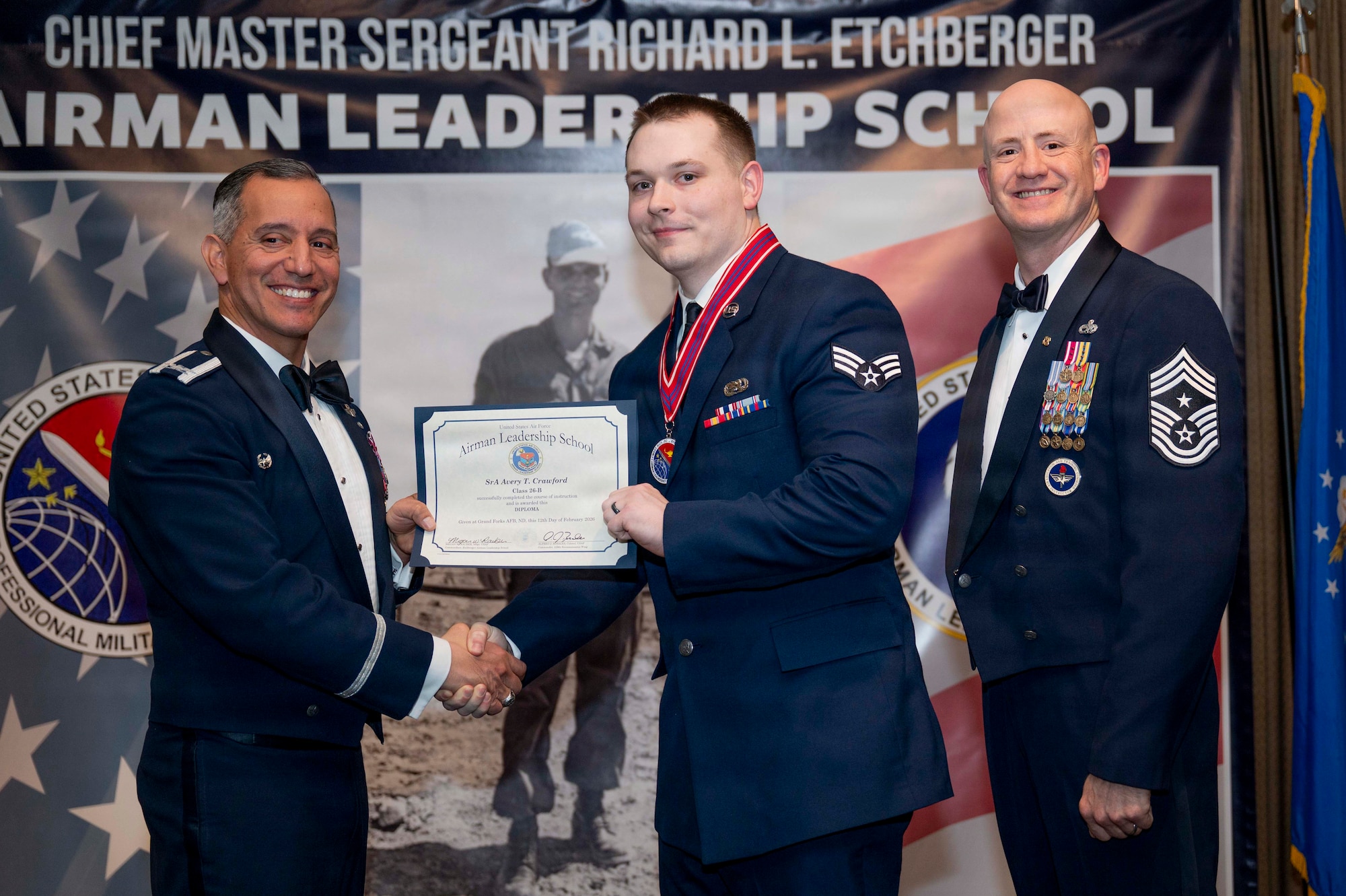 Col. Alfred Rosales, 319th Reconnaissance Wing commander, and Chief Master Sgt. William Gruenes, 319th RW command chief, presents Senior Airman Avery Crawford with an Airman Leadership School graduation certificate at Grand Forks Air Force Base, N.D., Feb. 12, 2026.