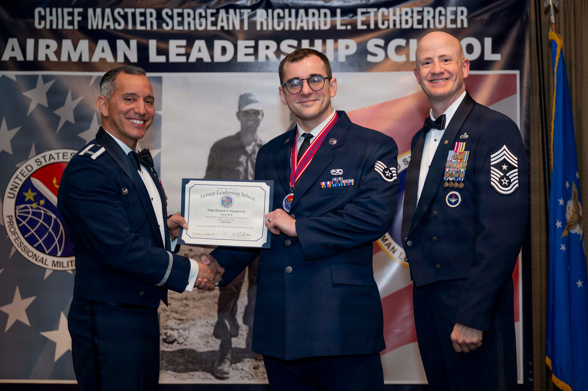 Col. Alfred Rosales, 319th Reconnaissance Wing commander, and Chief Master Sgt. William Gruenes, 319th RW command chief, presents Staff Sergeant Daniel Gasperich with an Airman Leadership School graduation certificate at Grand Forks Air Force Base, N.D., Feb. 12, 2026.