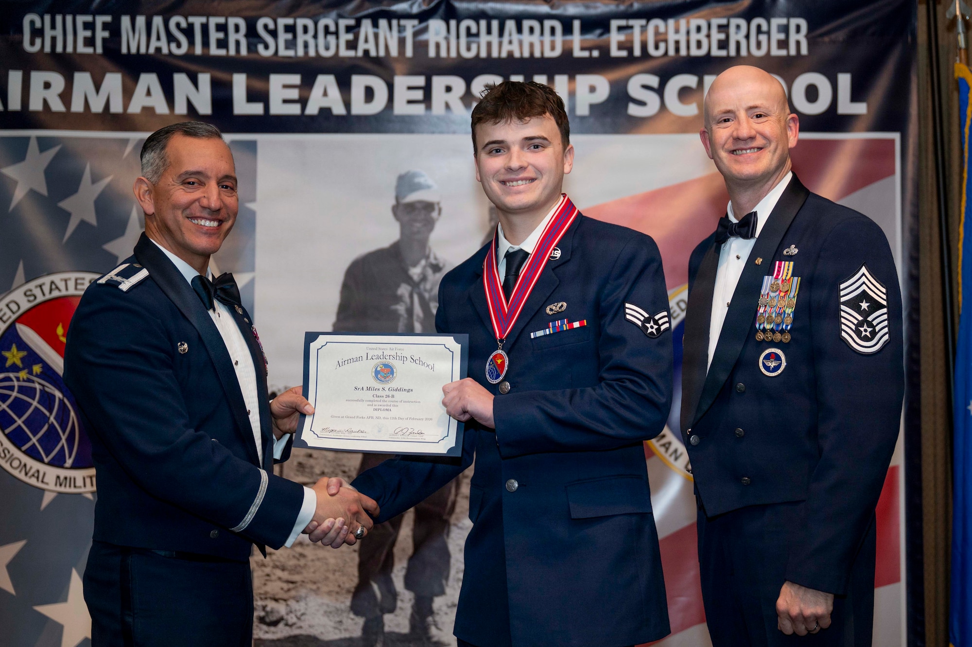 Col. Alfred Rosales, 319th Reconnaissance Wing commander, and Chief Master Sgt. William Gruenes, 319th RW command chief, presents Senior Airman Miles Giddings with an Airman Leadership School graduation certificate at Grand Forks Air Force Base, N.D., Feb. 12, 2026.