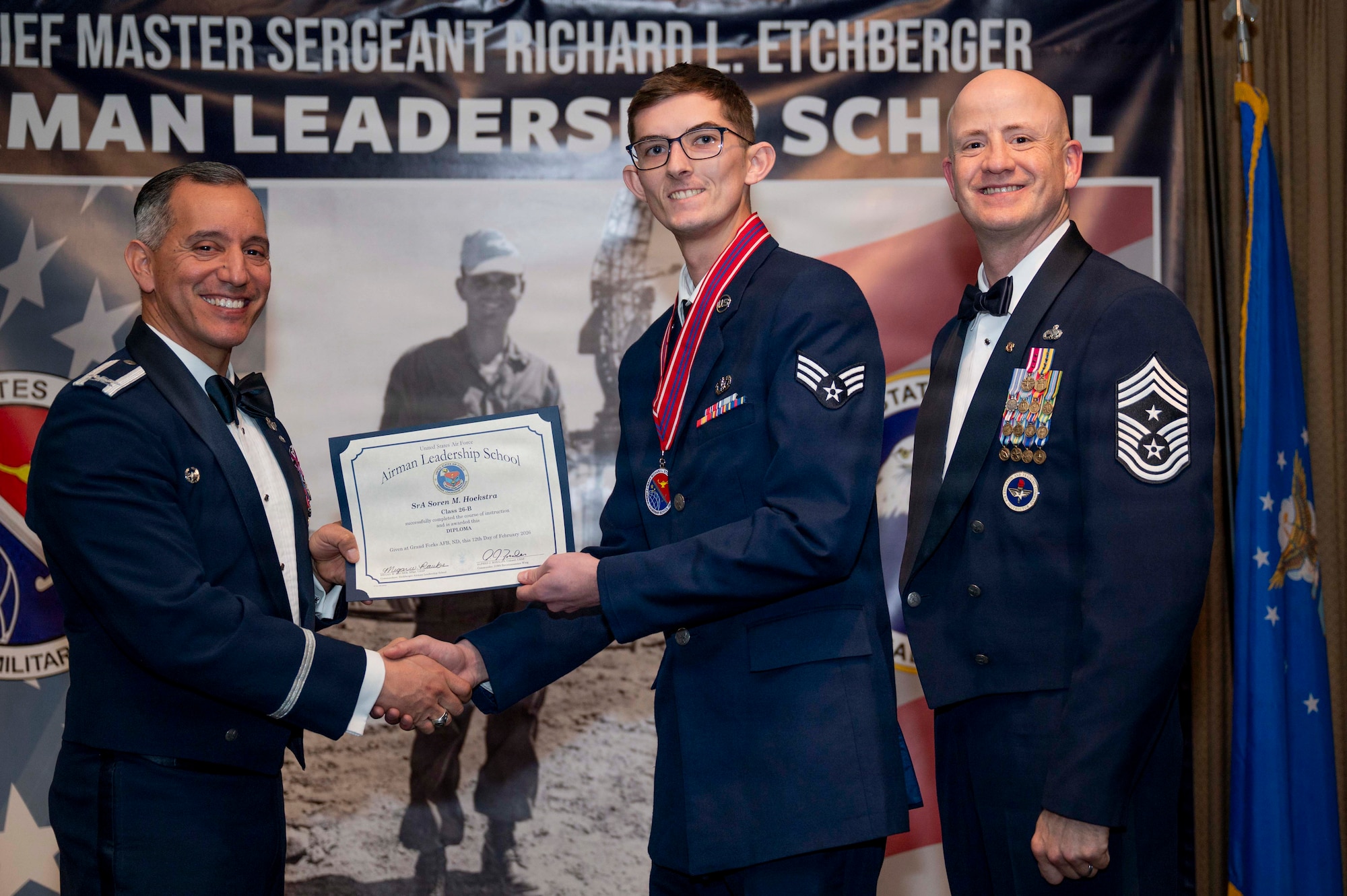 Col. Alfred Rosales, 319th Reconnaissance Wing commander, and Chief Master Sgt. William Gruenes, 319th RW command chief, presents Senior Airman Soren Hoekstra with an Airman Leadership School graduation certificate at Grand Forks Air Force Base, N.D., Feb. 12, 2026.
