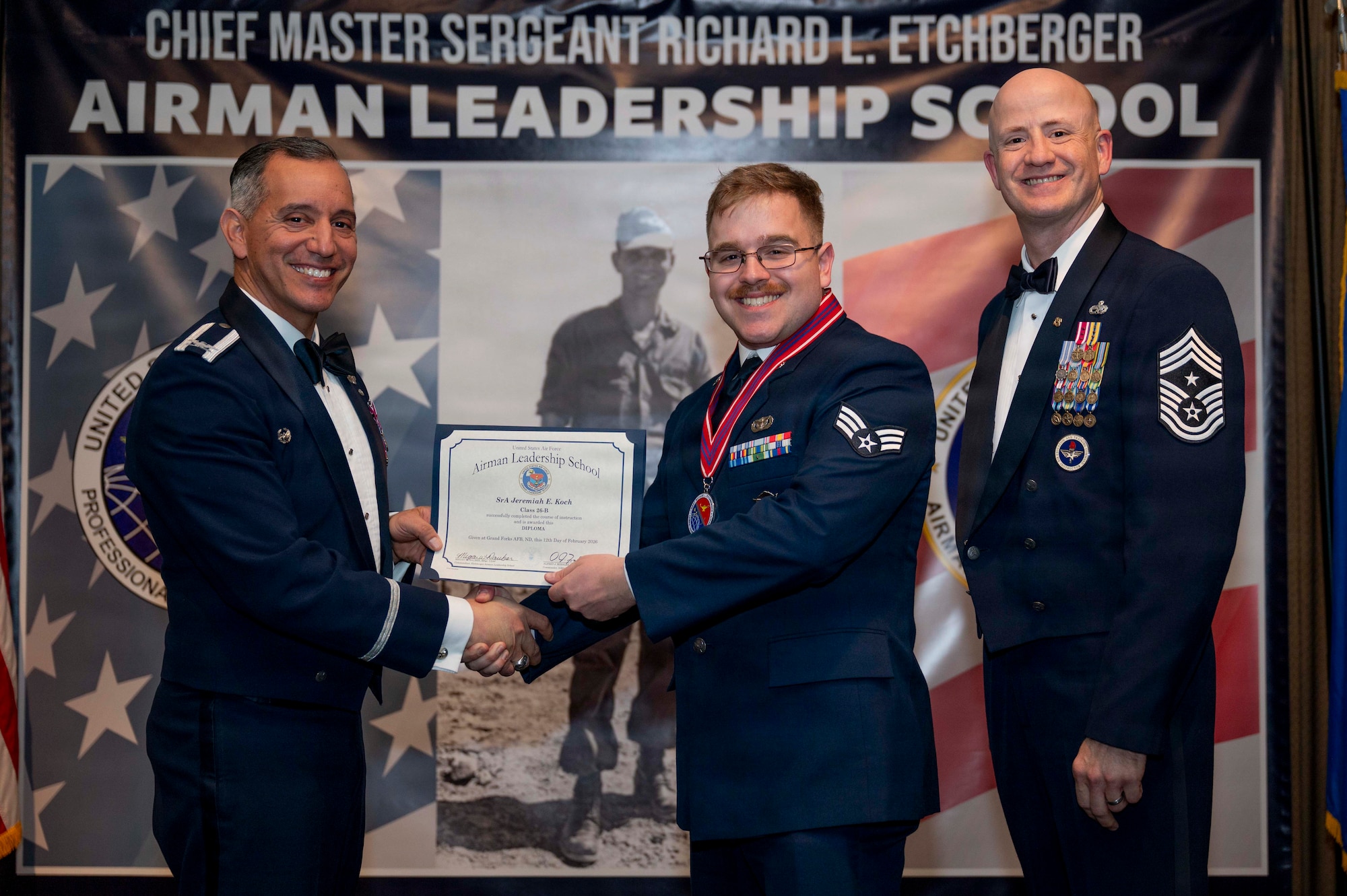 Col. Alfred Rosales, 319th Reconnaissance Wing commander, and Chief Master Sgt. William Gruenes, 319th RW command chief, presents Jeremiah Koch with an Airman Leadership School graduation certificate at Grand Forks Air Force Base, N.D., Feb. 12, 2026.
