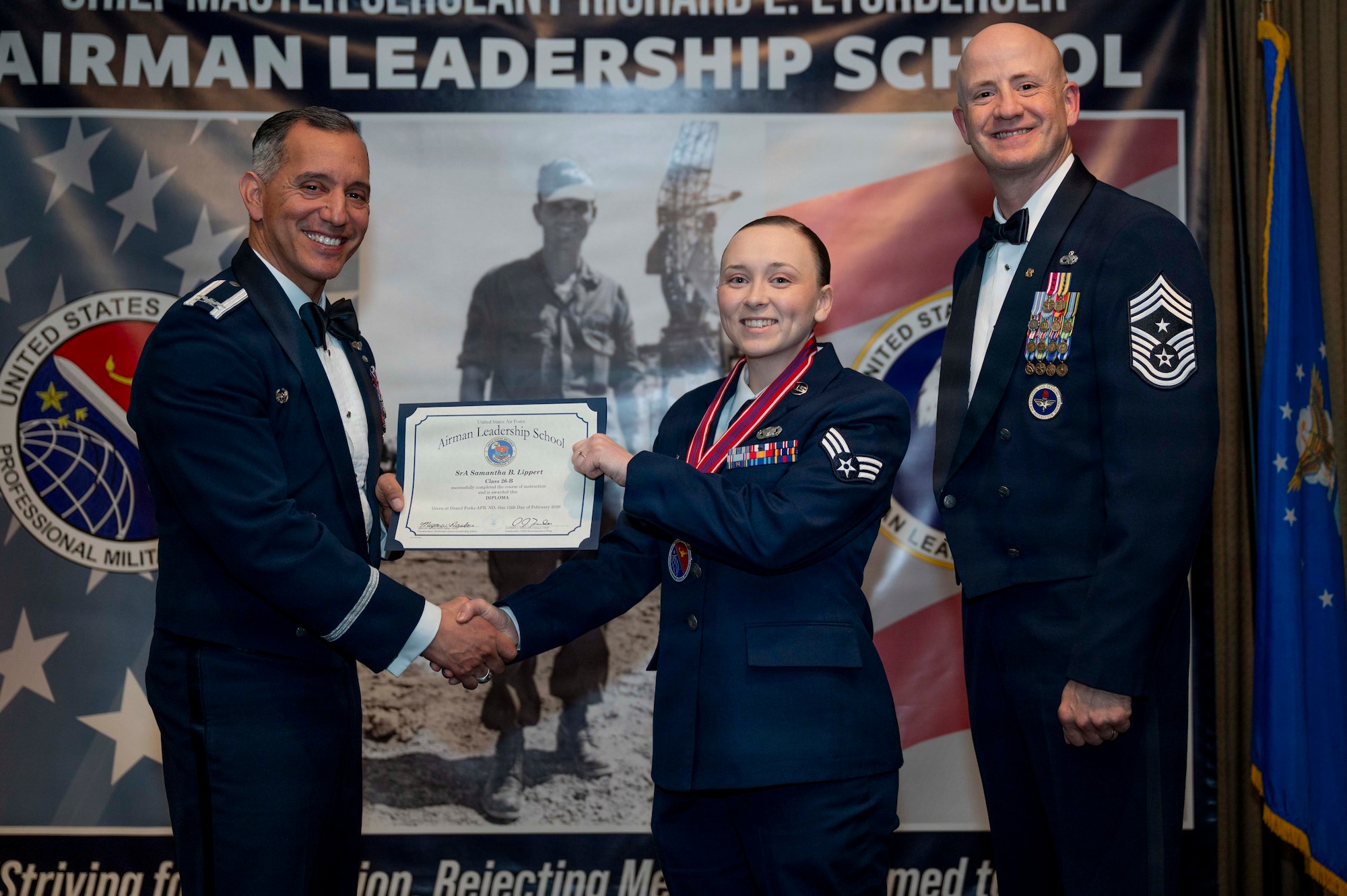 Col. Alfred Rosales, 319th Reconnaissance Wing commander, and Chief Master Sgt. William Gruenes, 319th RW command chief, presents Senior Airman Samantha Lippert with an Airman Leadership School graduation certificate at Grand Forks Air Force Base, N.D., Feb. 12, 2026.