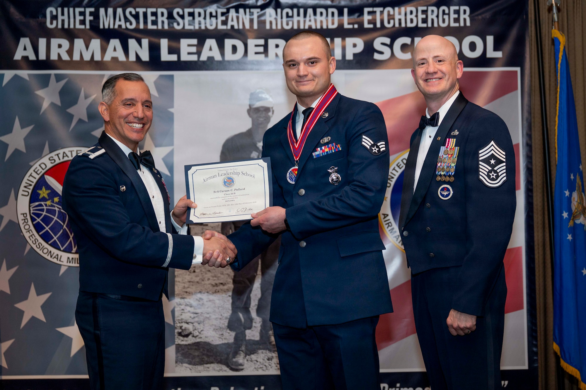 Col. Alfred Rosales, 319th Reconnaissance Wing commander, and Chief Master Sgt. William Gruenes, 319th RW command chief, presents Senior Airman Carson Pollard with an Airman Leadership School graduation certificate at Grand Forks Air Force Base, N.D., Feb. 12, 2026.