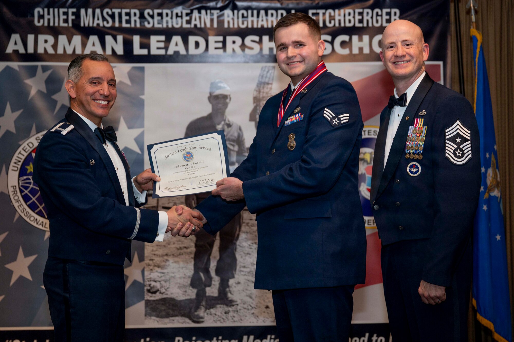 Col. Alfred Rosales, 319th Reconnaissance Wing commander, and Chief Master Sgt. William Gruenes, 319th RW command chief, presents Senior Airman Joseph Smart II with an Airman Leadership School graduation certificate at Grand Forks Air Force Base, N.D., Feb. 12, 2026.