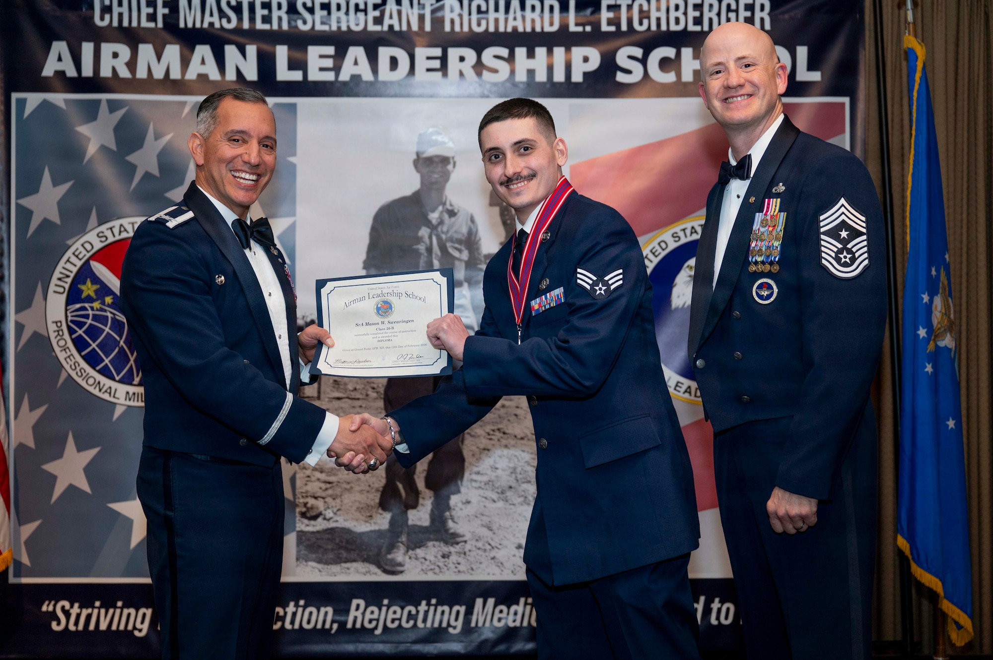 Col. Alfred Rosales, 319th Reconnaissance Wing commander, and Chief Master Sgt. William Gruenes, 319th RW command chief, presents Senior Airman Mason Swearingen with an Airman Leadership School graduation certificate at Grand Forks Air Force Base, N.D., Feb. 12, 2026.
