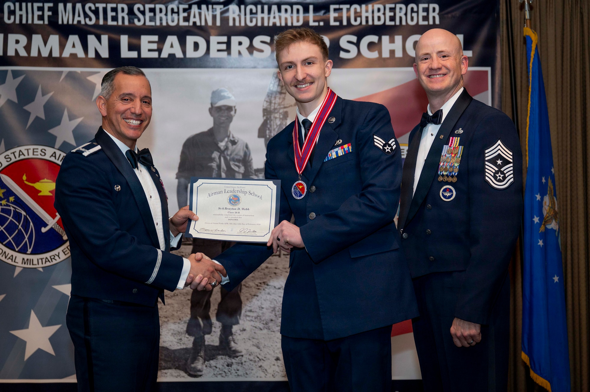 Col. Alfred Rosales, 319th Reconnaissance Wing commander, and Chief Master Sgt. William Gruenes, 319th RW command chief, presents Senior Airman Brayton Webb with an Airman Leadership School graduation certificate at Grand Forks Air Force Base, N.D., Feb. 12, 2026.