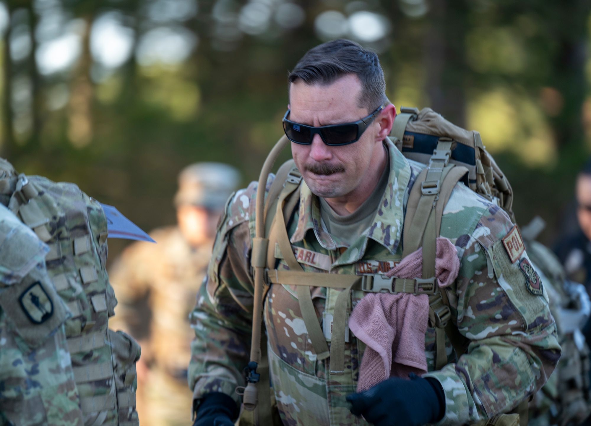 A uniformed service member jogs along a road carrying a large rucksack.