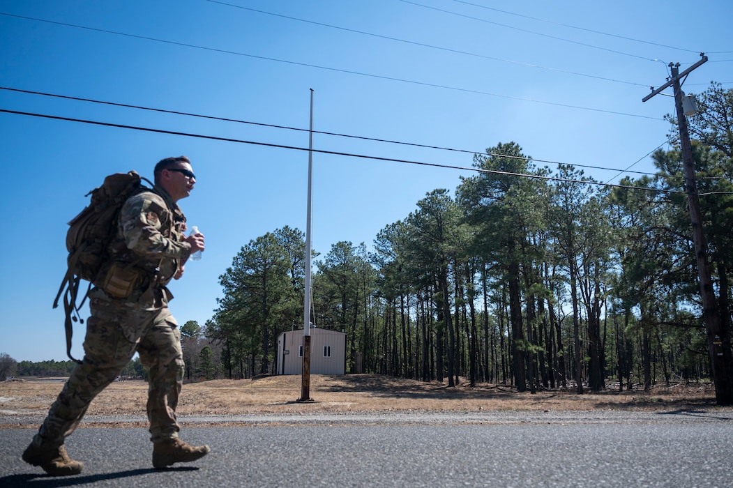 A uniformed service member jogs along a road carrying a large rucksack.