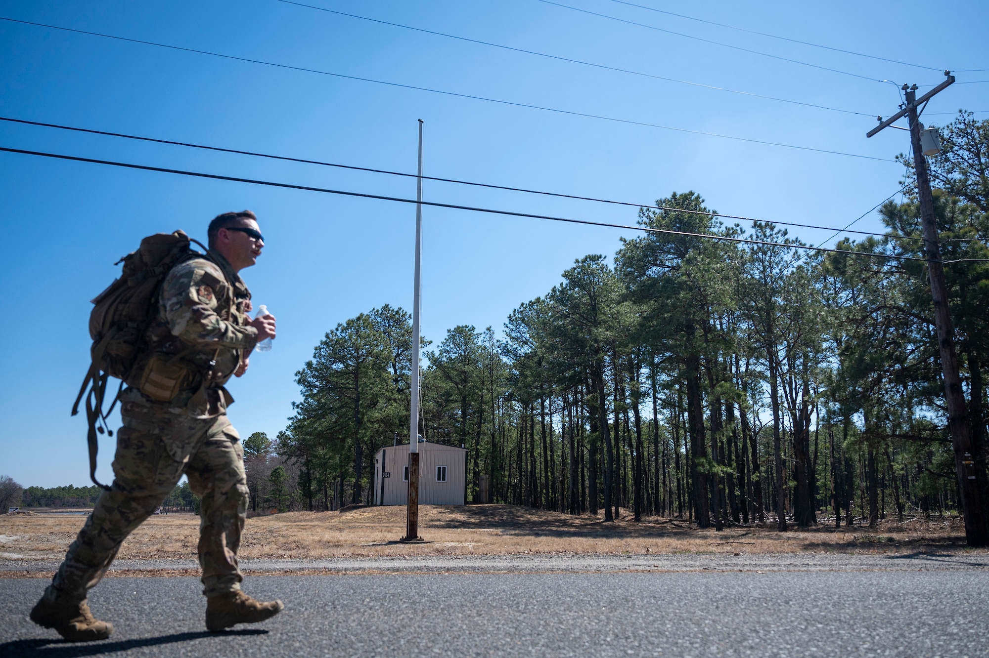 A uniformed service member jogs along a road carrying a large rucksack.