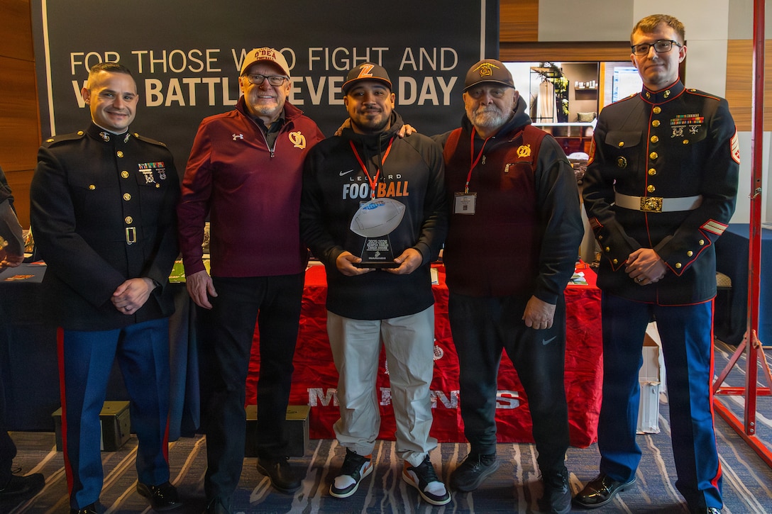 U.S. Marine Corps Maj. Patrick Kolb, left, commanding officer of Recruiting Station Seattle, and Staff Sgt. Ryan Peltz, right, a canvassing recruiter with Recruiting Sub-Station Covington, Recruiting Station Seattle, pose for a photograph with Anthony Espinoza, the recipient of the Semper Fi Coaching Award, during a Glazier Football Clinic in Renton, Washington, Feb. 21, 2026. Glazier Clinics is a coaching program designed for high school football coaches who are dedicated to improving as leaders and mentors and bettering their athletes (U.S. Marine Corps photo by Sgt. Bruin Largent)