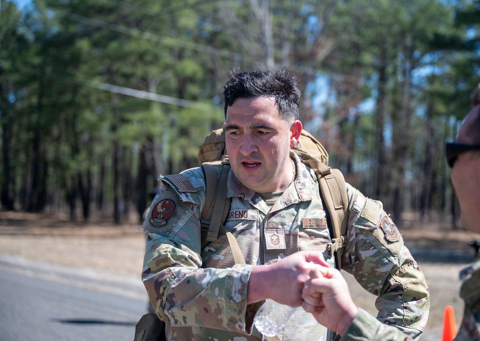 A uniformed service member jogs along a road carrying a large rucksack.