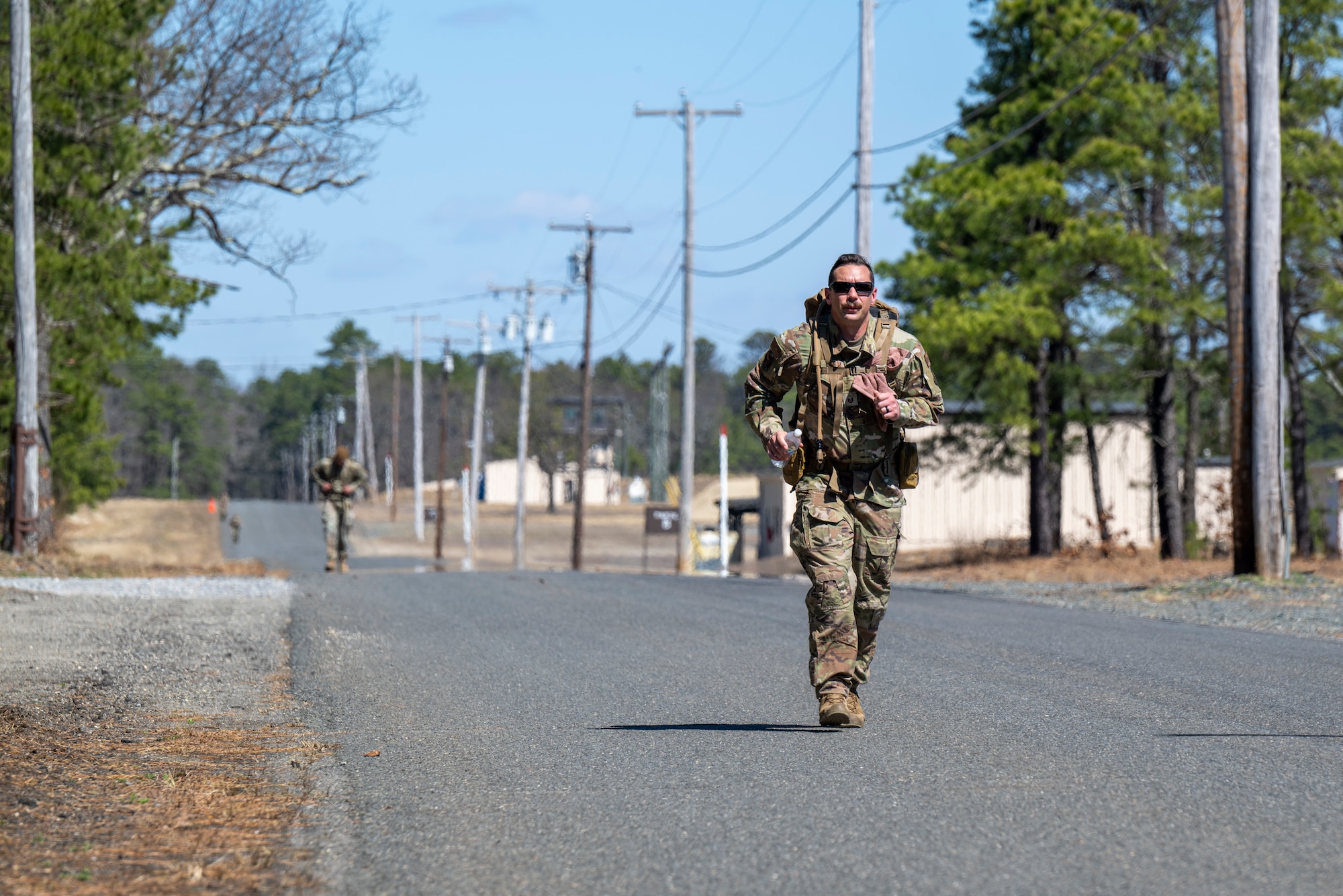 A uniformed service member jogs along a road carrying a large rucksack.