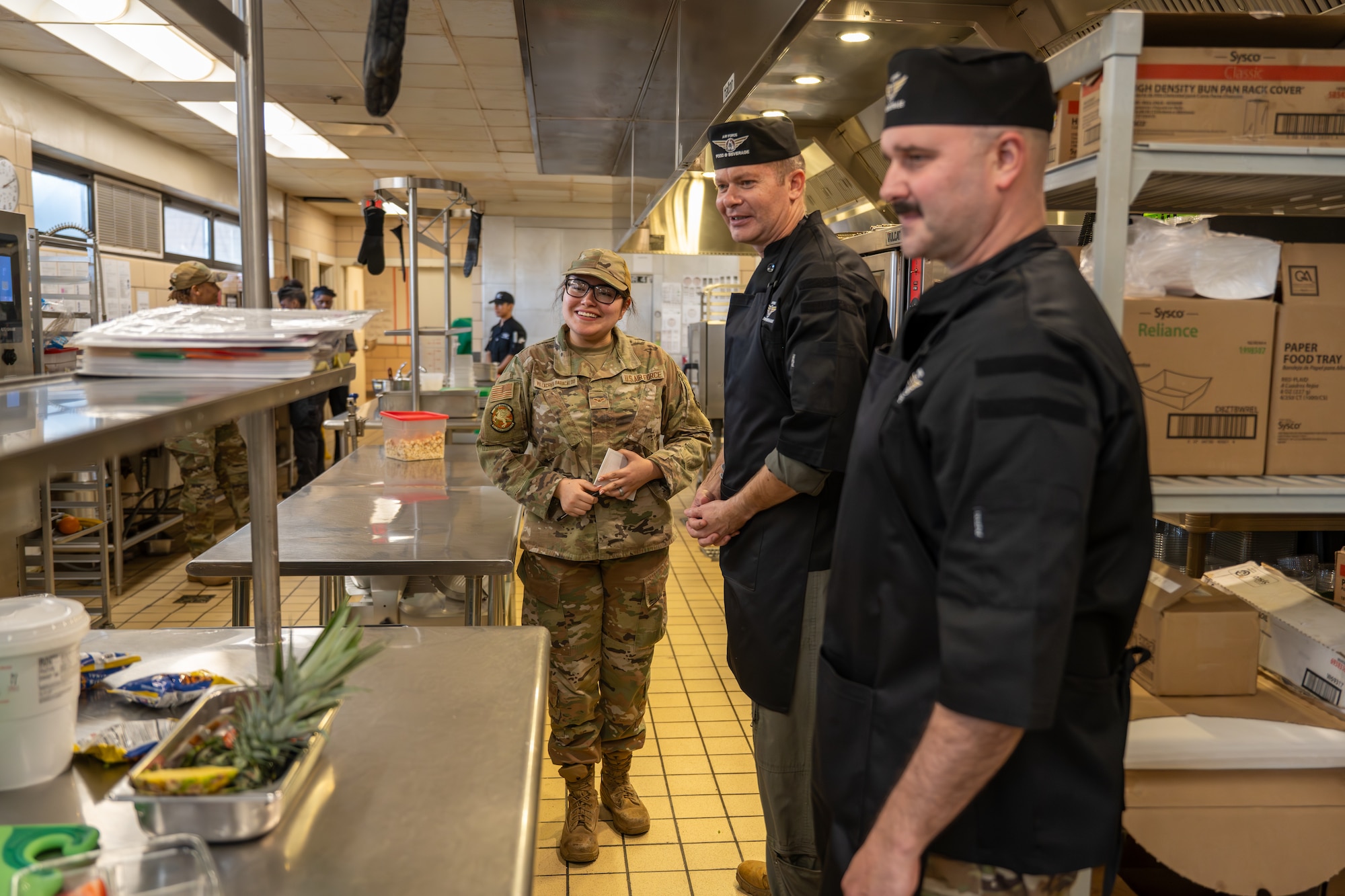 U.S. Air Force Col. Richard Kind, 97th Air Mobility Wing commander, center, Chief Master Sgt. Jonny Adams, 97th AMW command chief, right, are given a tour of the Hangar 97 dining facility by Airman 1st Class Sharon Villacres-Baracaldo, 97th Force Support Squadron dining facility accountant, left, at Altus Air Force Base, Oklahoma, March 23, 2026. The tour was part of the “Boots on the Ground” series, which gives the command team firsthand insight into critical base facilities. (U.S. Air Force photo by Airman 1st Class Nathan Langston)