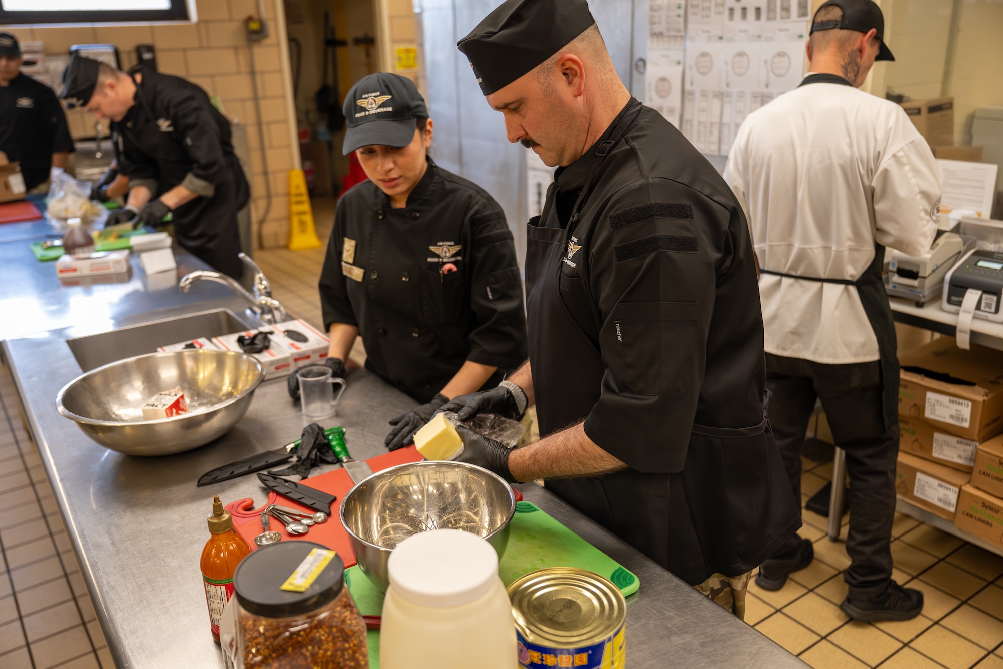 U.S. Air Force Chief Master Sgt. Jonny Adams, 97th Air Mobility Wing command chief, right, and Airman 1st Class Mia Franco, 97th Force Support Squadron dining facility shift worker, left, prepare sauce ingredients during an immersion tour at Altus Air Force Base, Oklahoma, March 23, 2026. The command team took part in a friendly cooking competition to learn more about how the 97th Force Support Squadron dining facility operates. (U.S. Air Force photo by Airman 1st Class Nathan Langston)