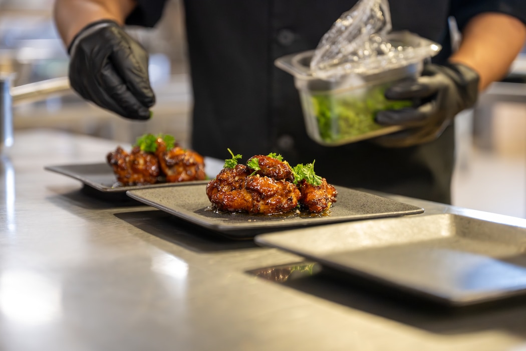 Chicken wings are seasoned with cilantro by U.S. Air Force Airman 1st Class Jonathan Cobaxin, 97th Force Support Squadron dining facility shift worker, during a hands-on “Boots on the Ground” immersion tour with the command team at Altus Air Force Base, Oklahoma, March 23, 2026. Col. Richard Kind, 97th Air Mobility Wing (AMW) commander, and Chief Master Sgt. Jonny Adams, 97th AMW command chief, prepared the wings as part of the event. (U.S. Air Force photo by Airman 1st Class Nathan Langston)