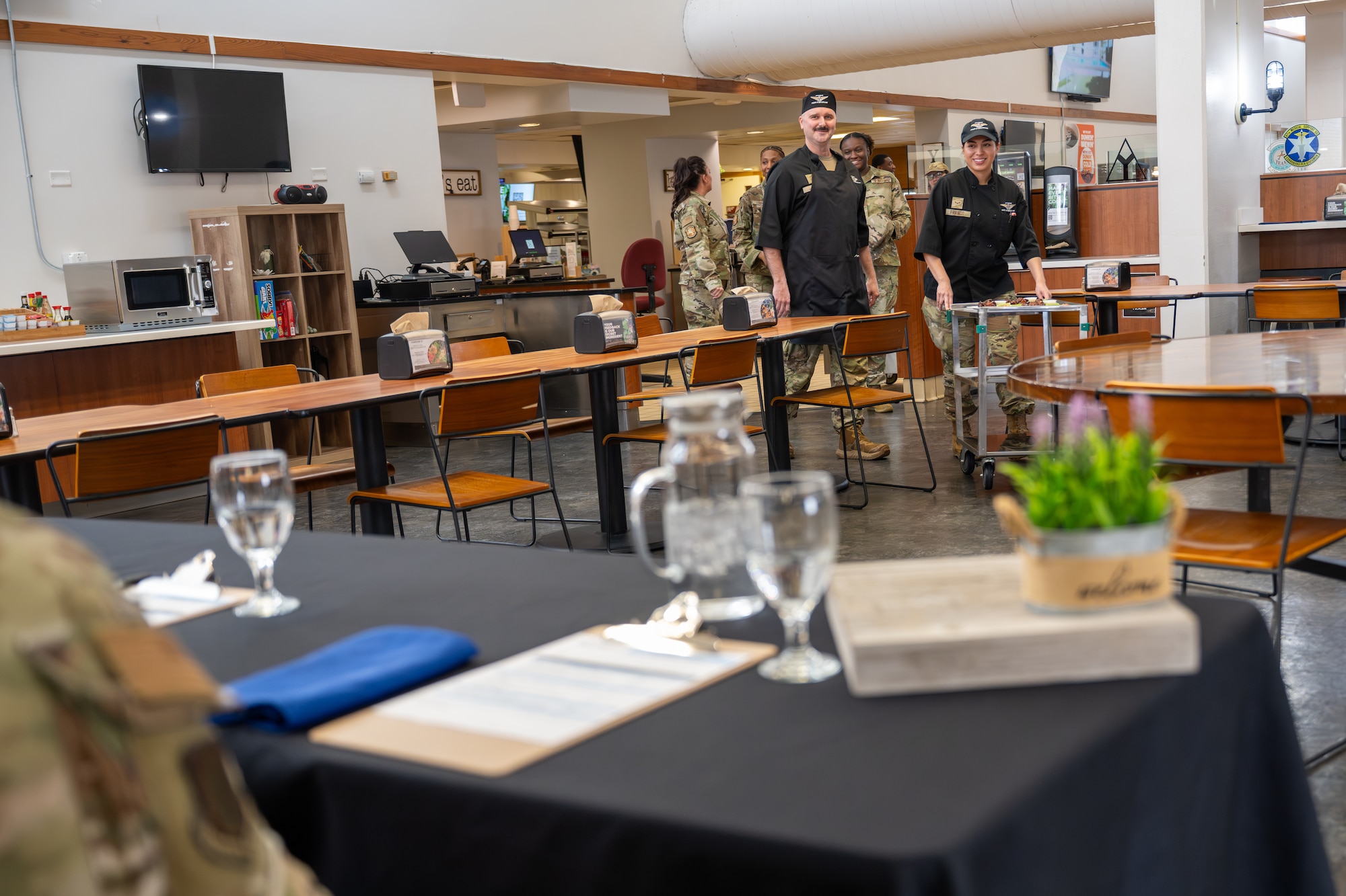 U.S. Air Force Chief Master Sgt. Jonny Adams, 97th Air Mobility Wing command chief (left), and Airman 1st Class Mia Franco, 97th Force Support Squadron dining facility shift worker (right), present chicken wings to judges during an immersion tour competition at Altus Air Force Base, Oklahoma, March 23, 2026. Members of the command team’s front office judged the wings using criteria provided by the 97th Force Support Squadron. (U.S. Air Force photo by Airman 1st Class Nathan Langston)