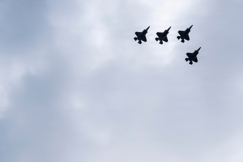 Four military fighter aircraft fly overhead.