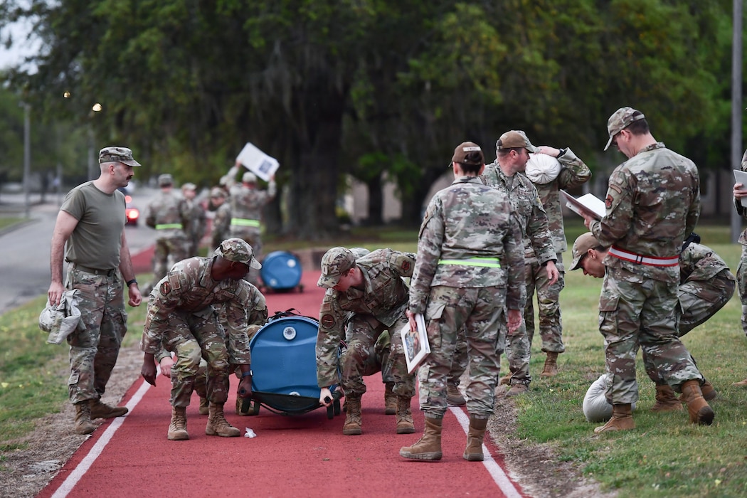A group of people in military uniform work together to lift a blue barrel.