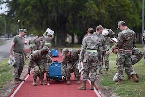 A group of people in military uniform work together to lift a blue barrel.