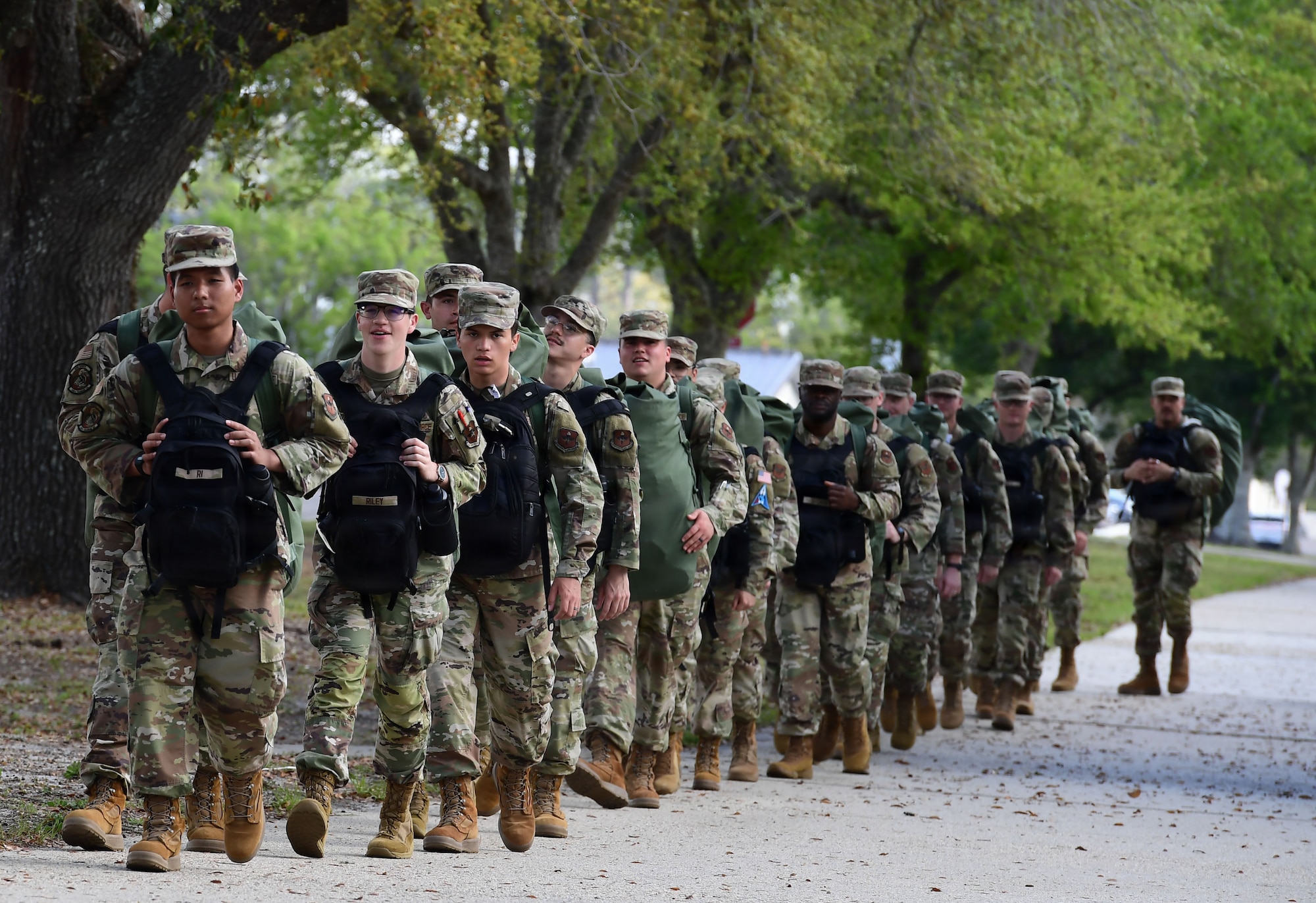 A group of military members carry back backs while marching in formation.