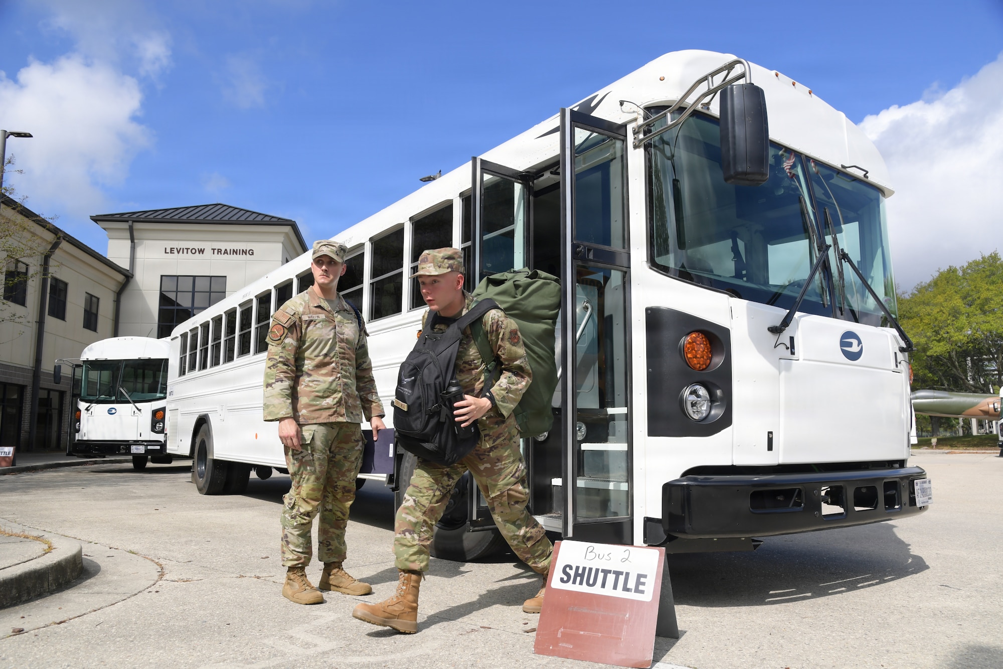 A military member walks off of a bus carrying a backpack